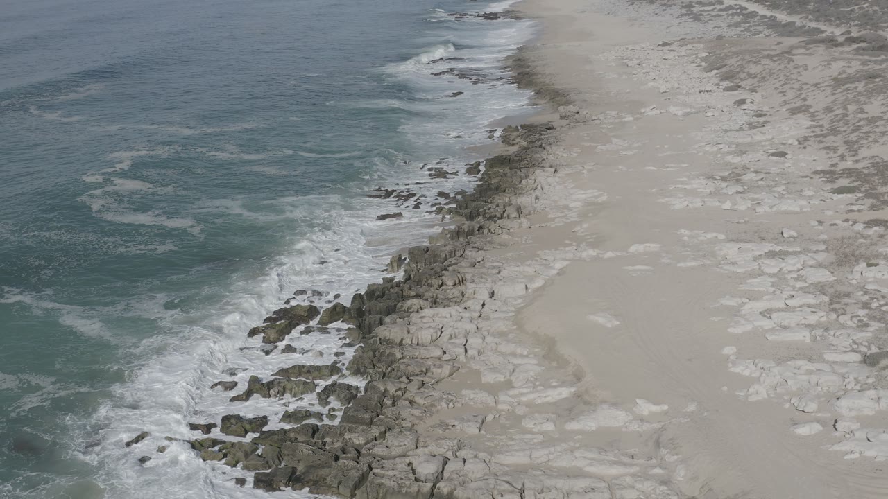 Rocky beach edge with foamy surf and pale sand.