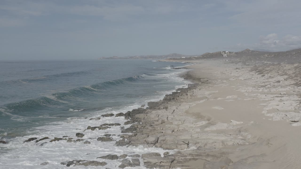Ocean swell nearing rocks along a sandy coast