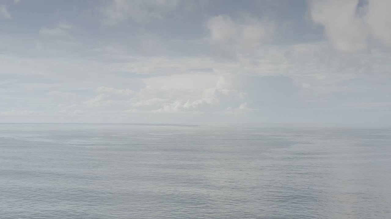 Los Cabos ocean horizon under a layered cloudy sky, with pale rippled water below and no visible people.