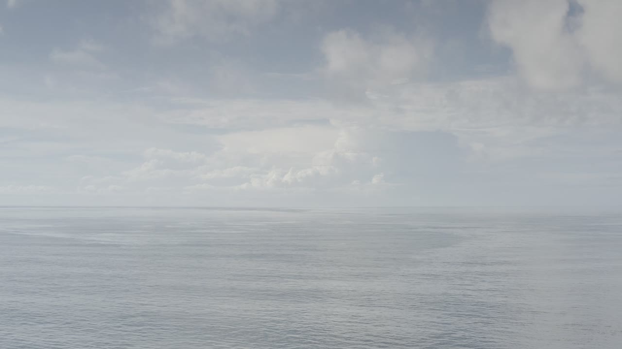 Opening frame of calm ocean water in Los Cabos, Mexico, with a pale horizon, layered gray clouds, and no visible people.