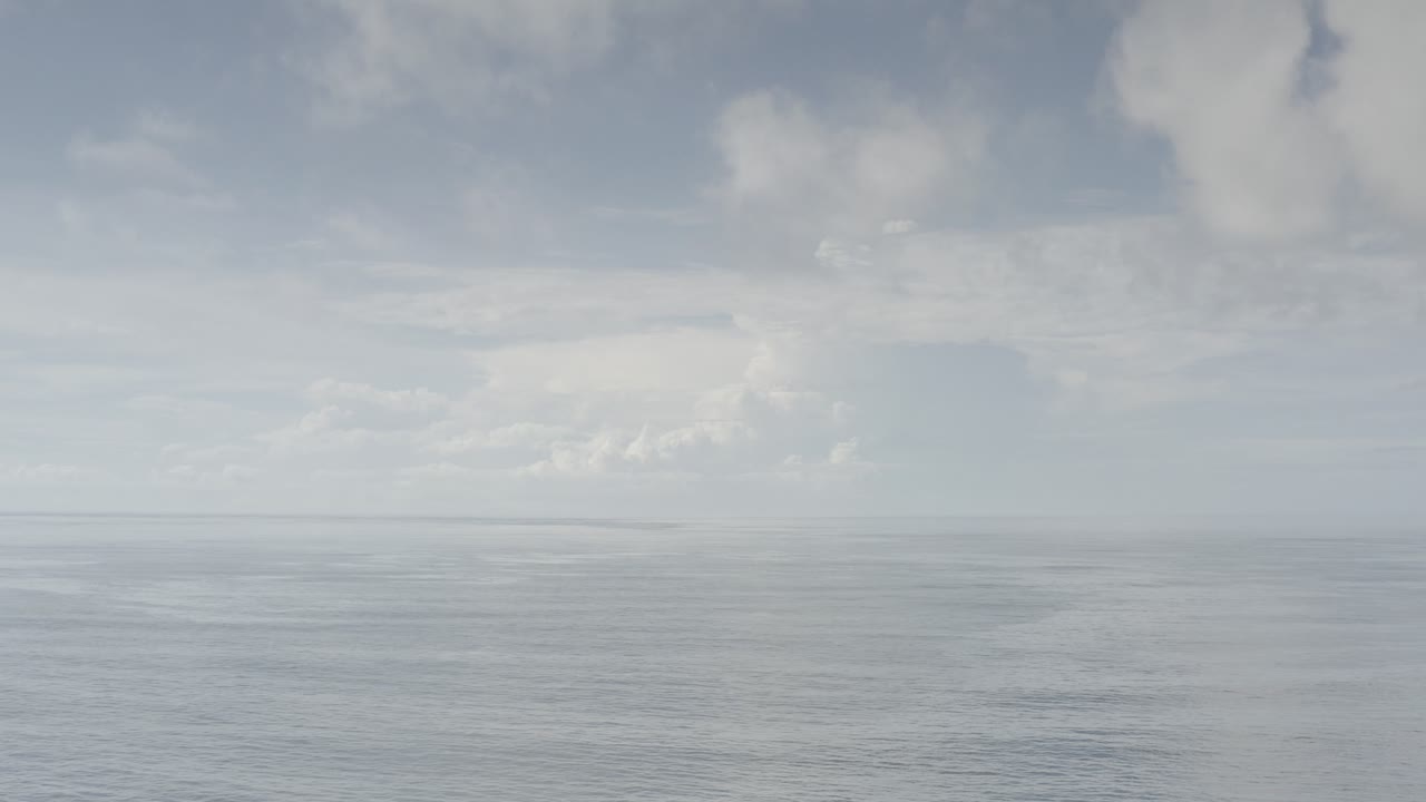 Opening frame of the Los Cabos, Mexico clip showing a pale blue sky, soft white clouds, and a calm ocean horizon with no visible people.