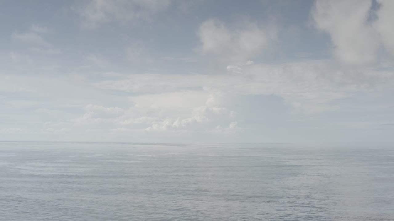Opening frame of a Los Cabos, Mexico aerial view with pale ocean below a band of soft white clouds and no visible people.