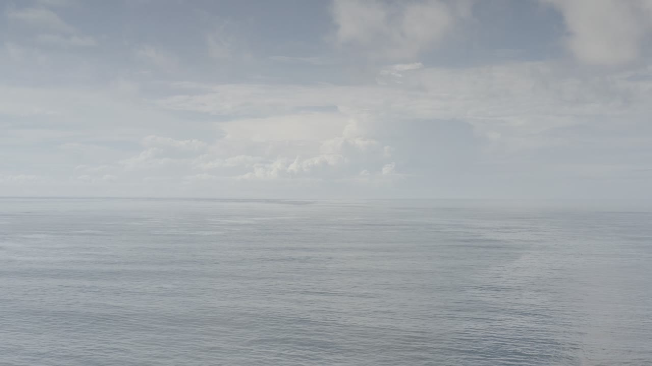 Pale ocean horizon under a cloudy white-blue sky.