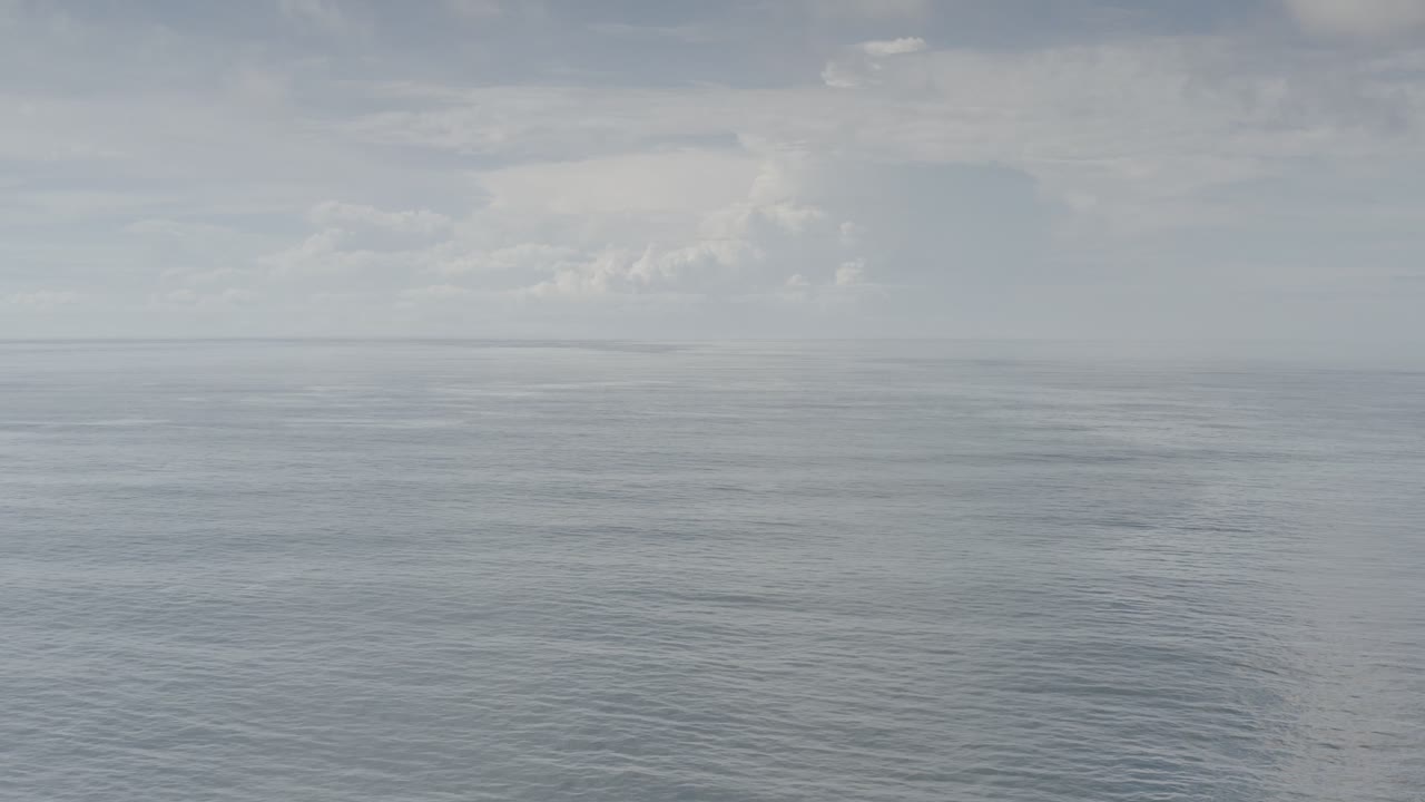 Distant horizon over calm ocean with scattered cloud formations.