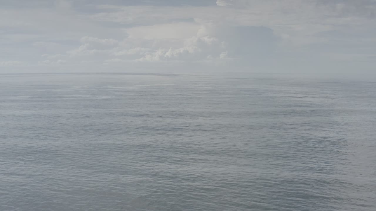 A pale cloudy sky hangs over flat open water in Los Cabos, Mexico, with the horizon softened by haze and no visible people.