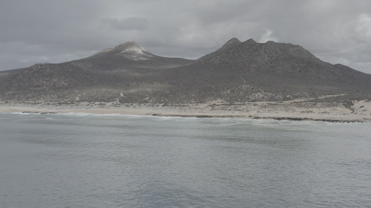 Aerial view of gray ocean, sandy beach, and dark coastal mountains.