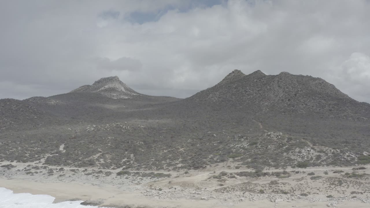 Cloudy coastal mountains above scrubland and pale sand