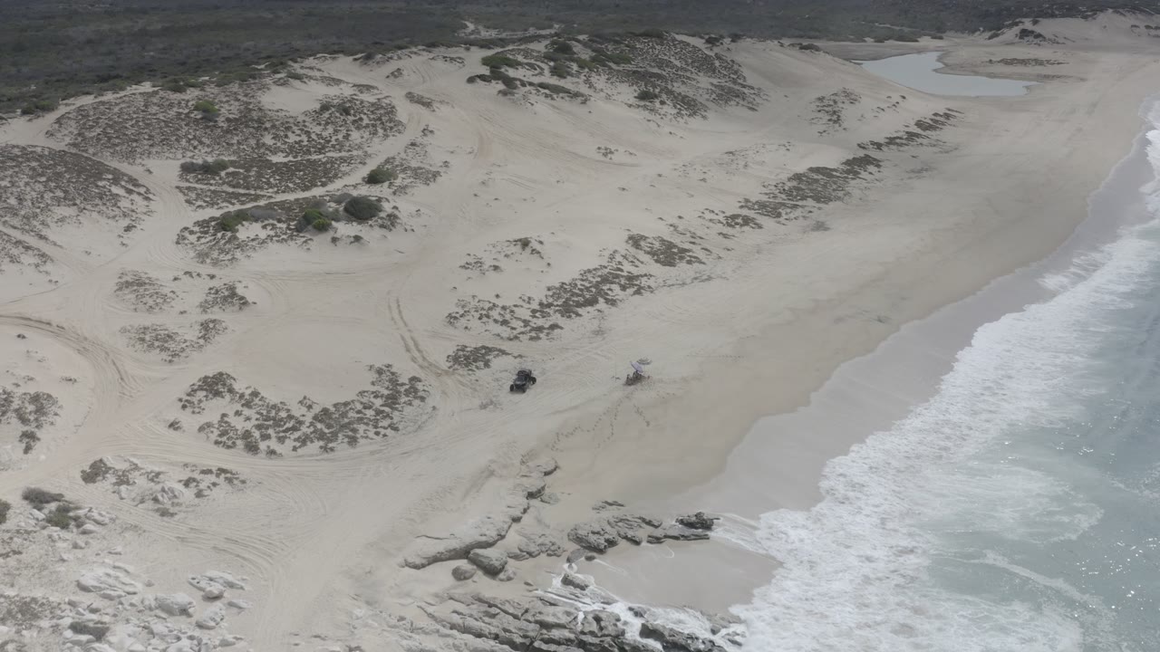 Drone view of sandy dunes and ocean foam along the beach