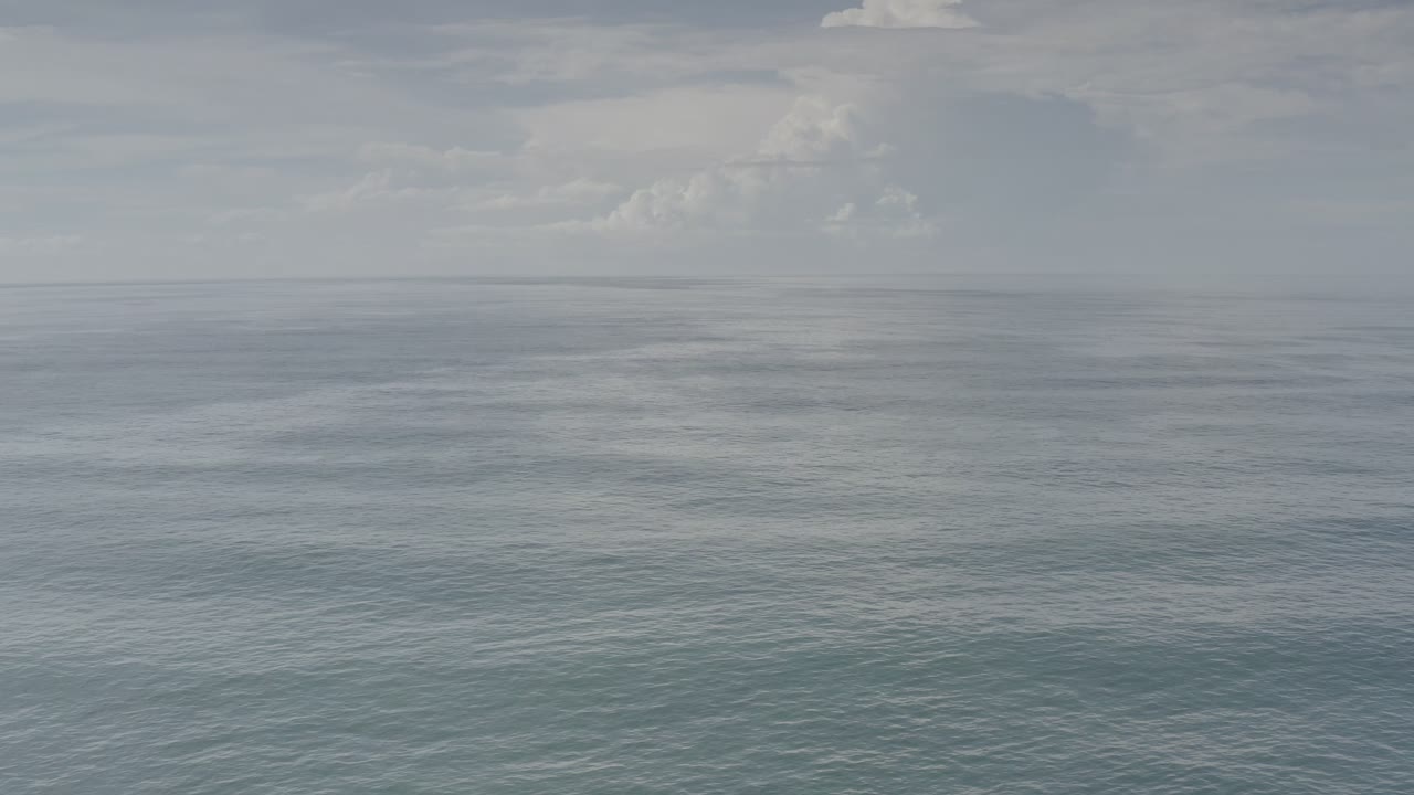 Aerial Los Cabos ocean view with muted blue-gray water, a distant level horizon, dense clouds overhead, and no visible people.