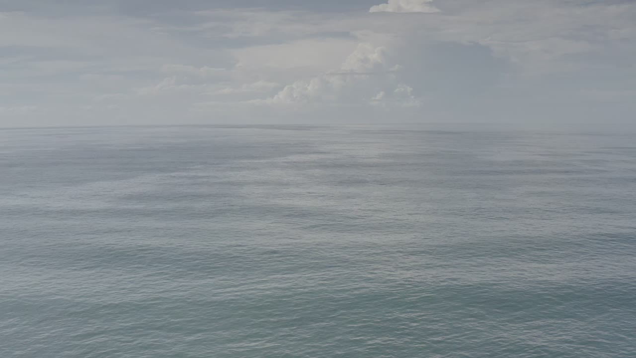A wide aerial frame over Los Cabos water shows faint surface texture, low contrast cloud cover, a pale horizon line, and no visible people.