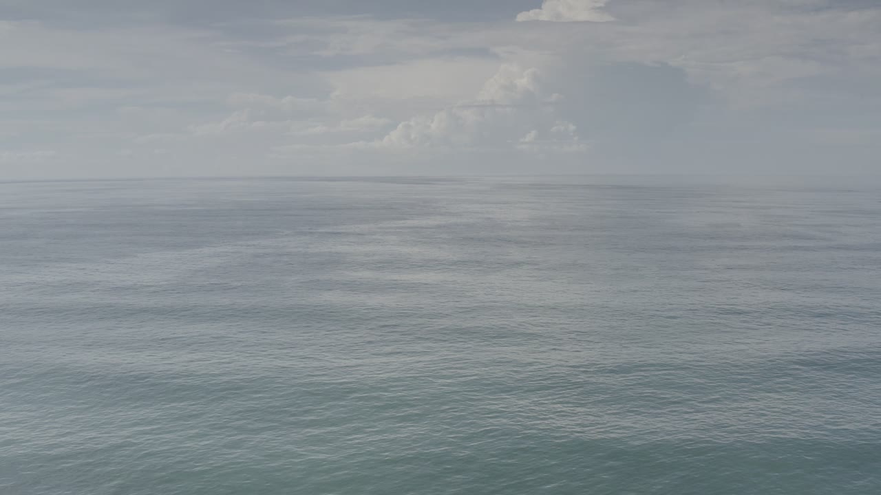 Los Cabos ocean water fills most of the frame while a low band of cloud sits above the distant horizon, with no visible people.