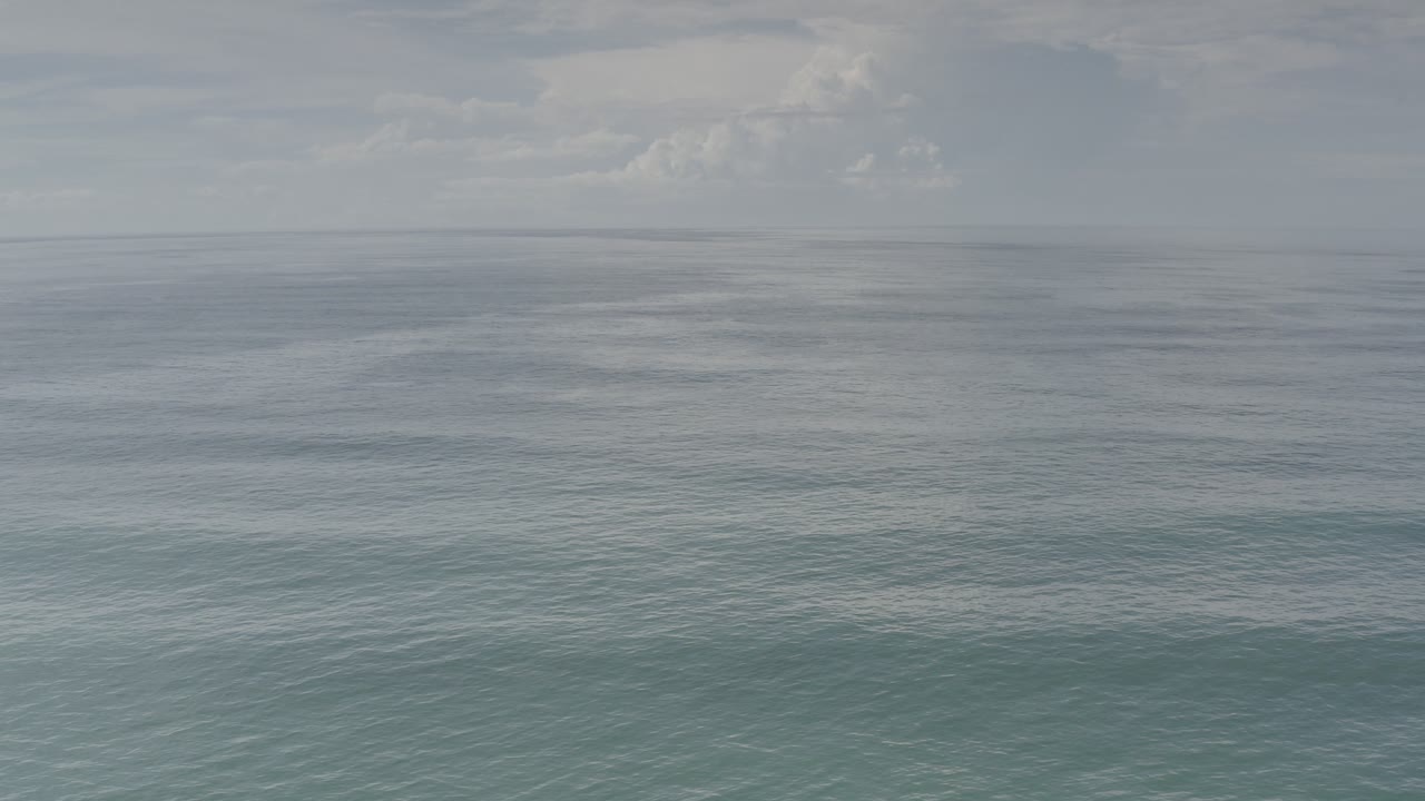 Wide view over the ocean in Los Cabos, Mexico, with muted blue-green water, a level horizon, distant cloud cover, and no visible people.