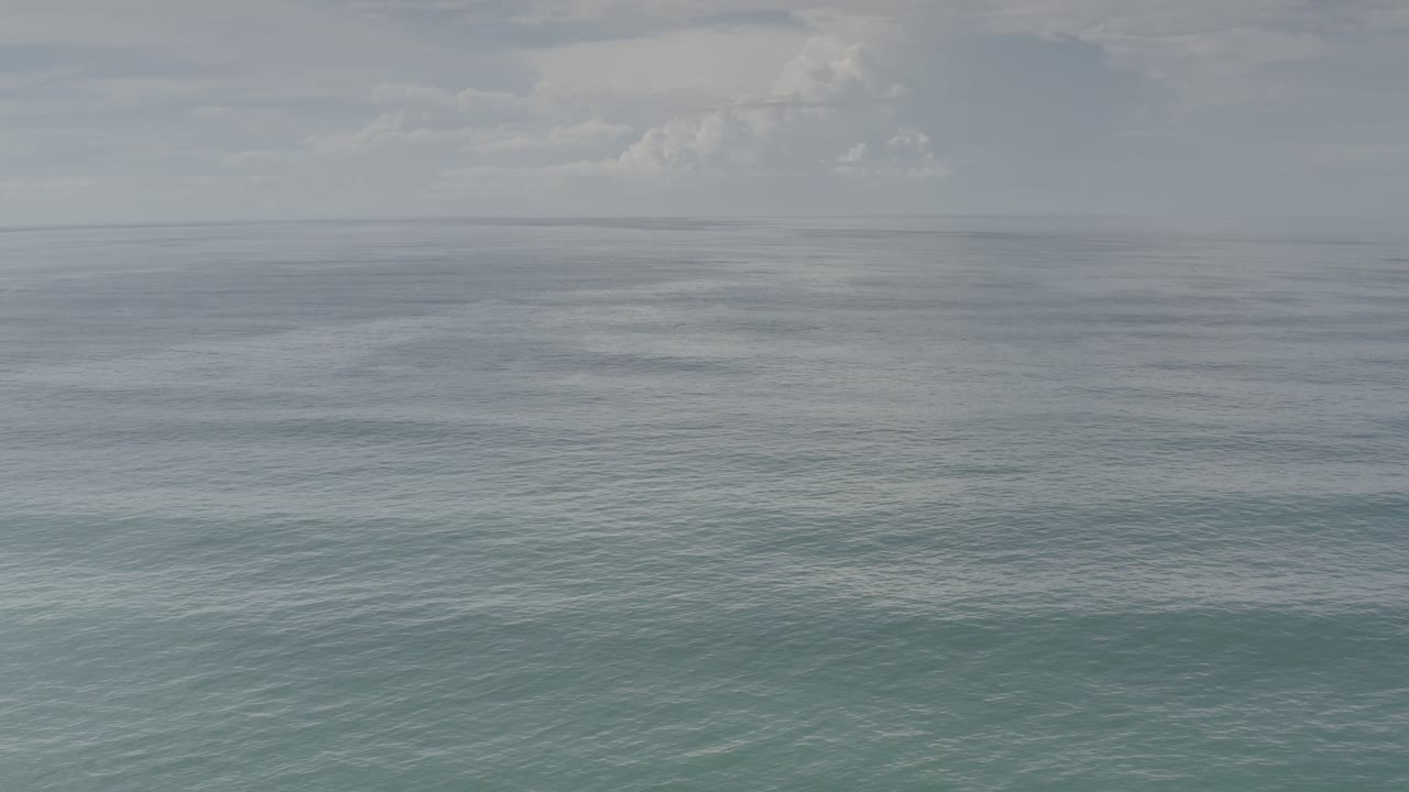Blue-green ocean surface under a hazy clouded sky.