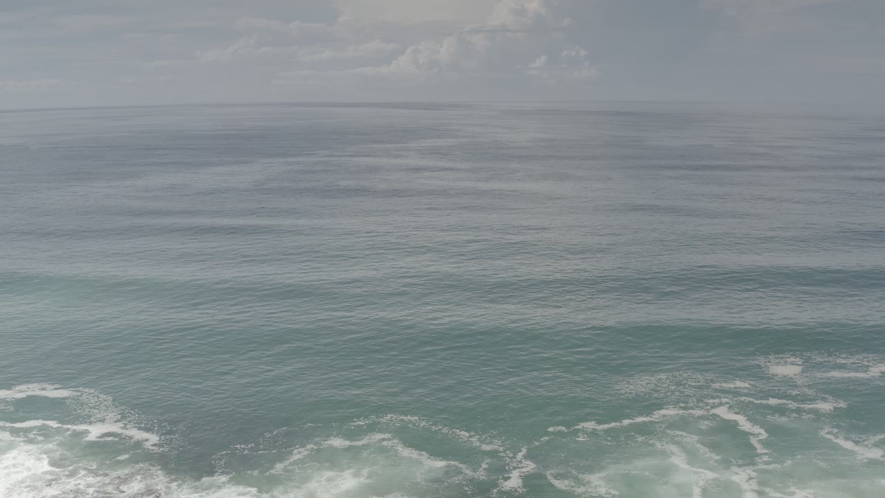 Wide aerial view of choppy ocean with white foam near shore.