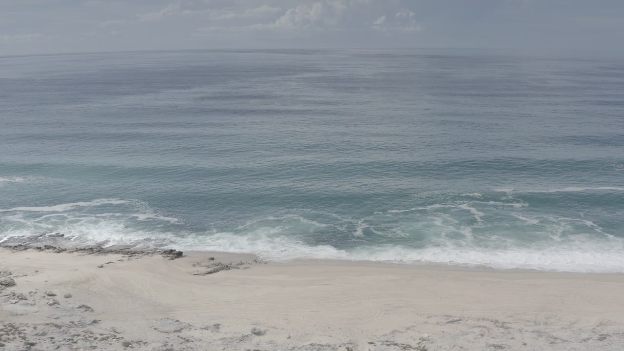 Opening frame of a Los Cabos beach with pale sand below blue-green surf and a distant ocean horizon, with no visible people.