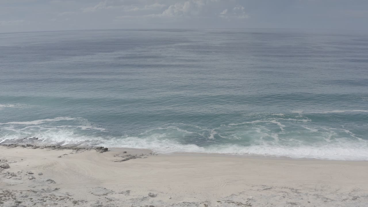 Los Cabos shoreline view with white wave foam spreading across the beach and open ocean beyond, with no visible people.