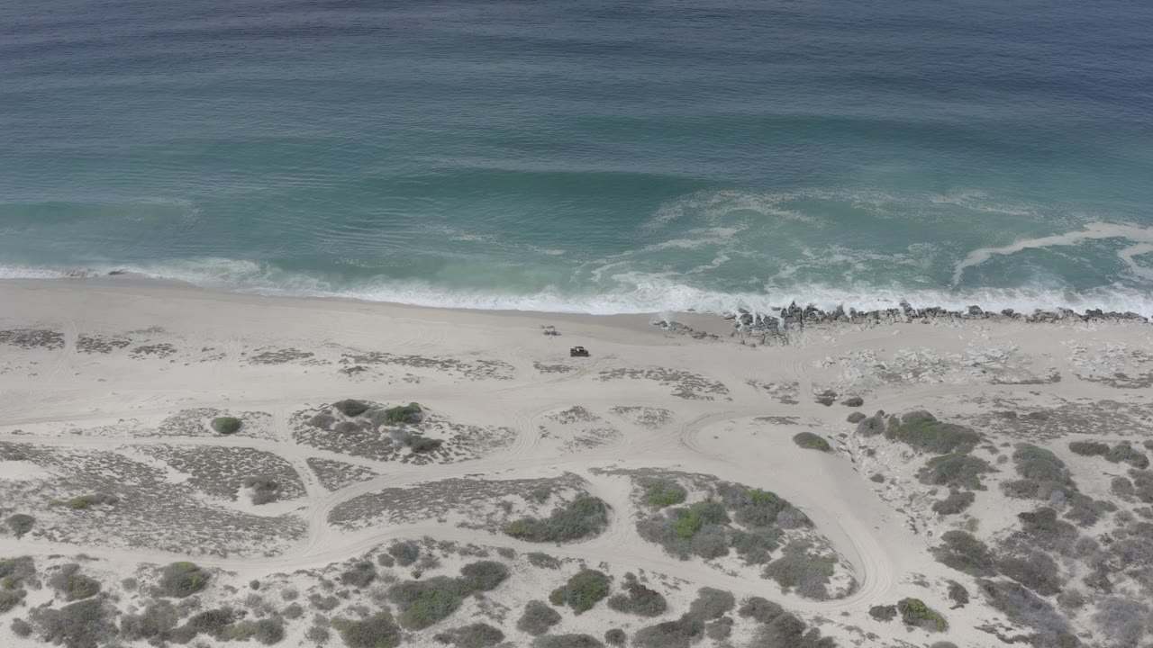 Aerial view of sand dunes, beach, surf, and blue ocean.