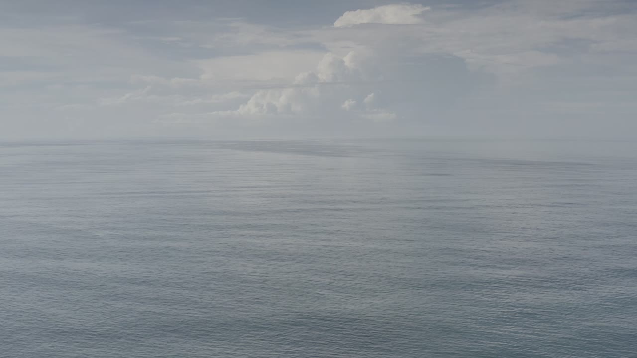 Calm Los Cabos, Mexico sea stretches toward a low horizon, with layered pale clouds and no visible people.