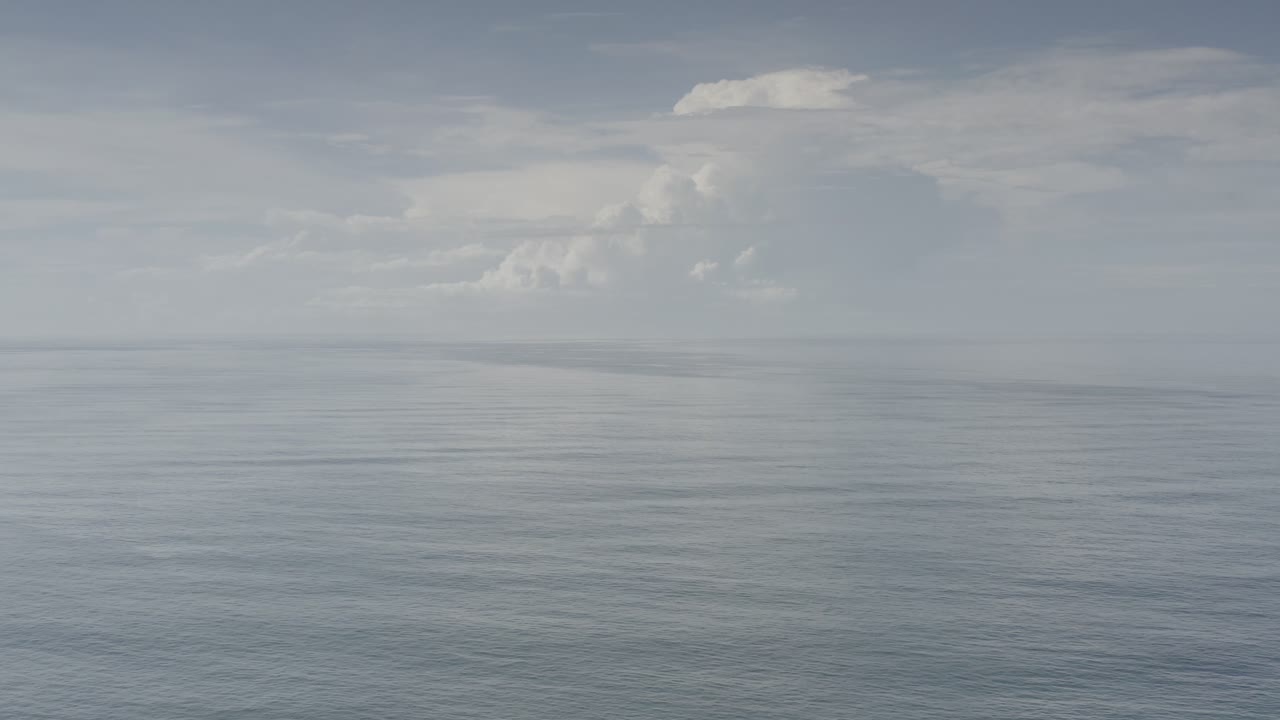 Los Cabos ocean view one second in, with a broad pale water surface, a straight horizon, soft clouds, and no visible people.