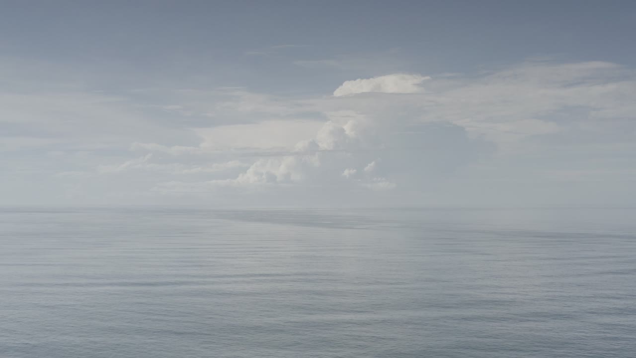 Wide Los Cabos ocean horizon beneath a pale gray-blue sky with large white cloud banks and no visible people.