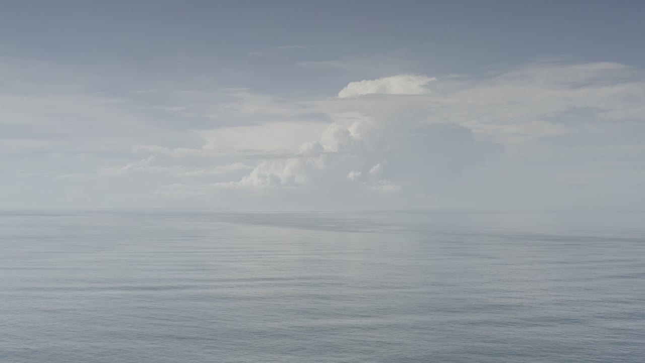 Los Cabos waterline sits low in frame while broad white and gray clouds spread across the pale sky, with no visible people.