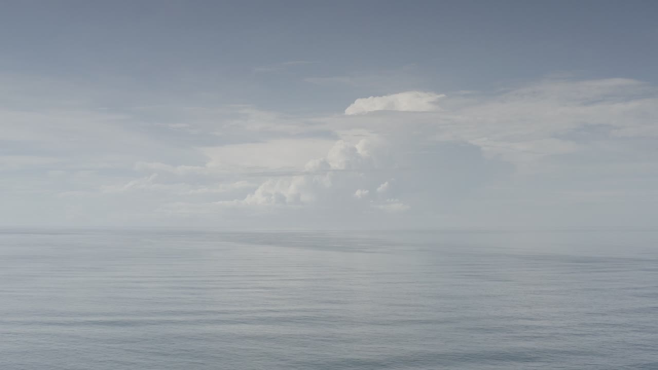 Calm ocean horizon beneath a large pale cloud formation.