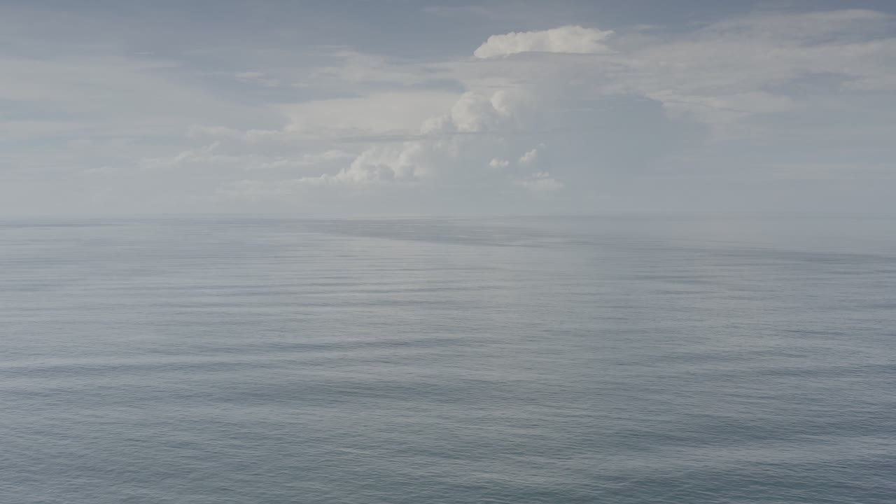 Wide ocean horizon beneath a pale cloudy sky.