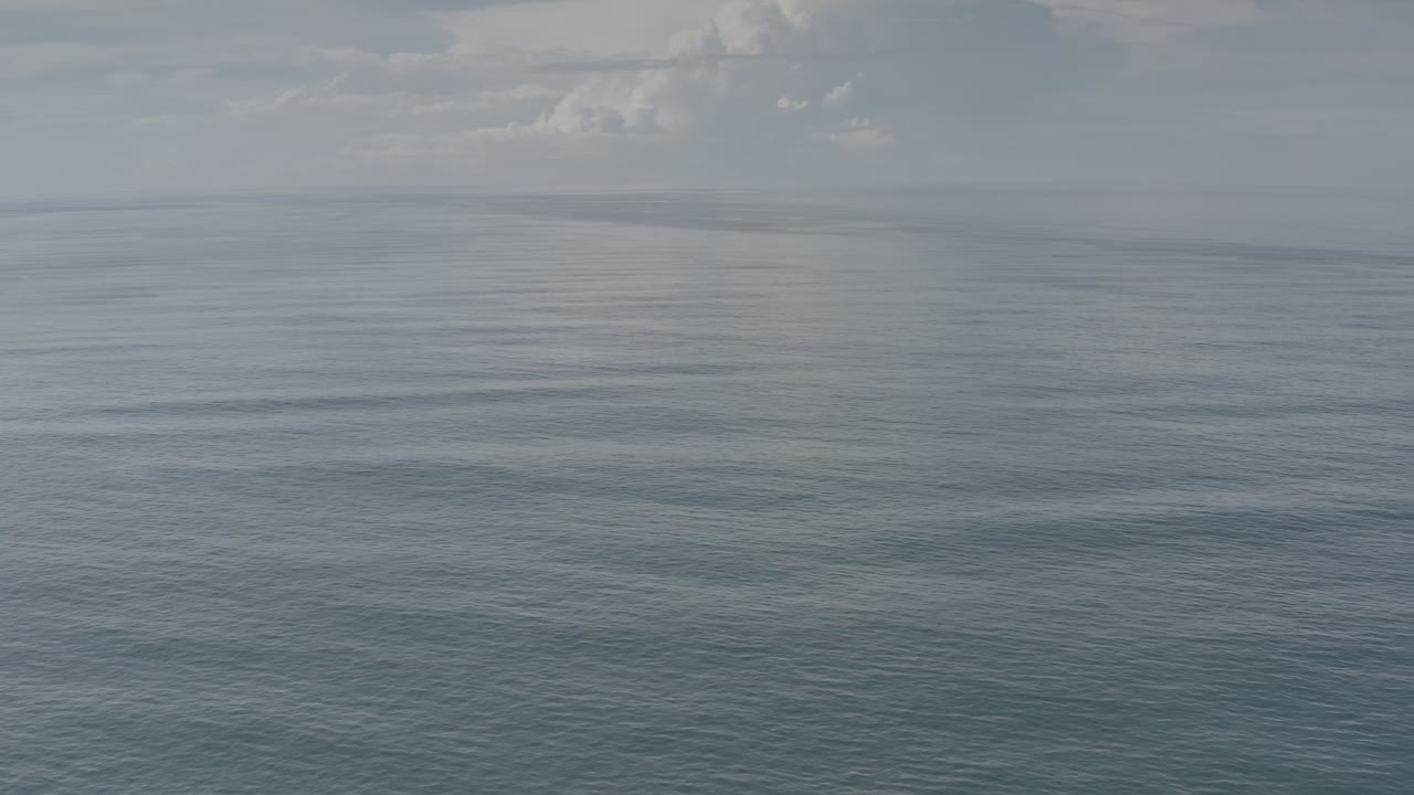 Los Cabos ocean surface fills most of the frame, with fine ripples, a pale cloudy sky, and no visible people.