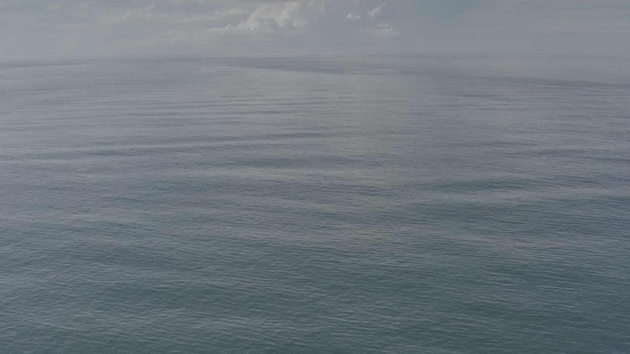 Opening frame of blue-green ocean in Los Cabos, Mexico, with small ripples, a level horizon, pale clouds, and no visible people.