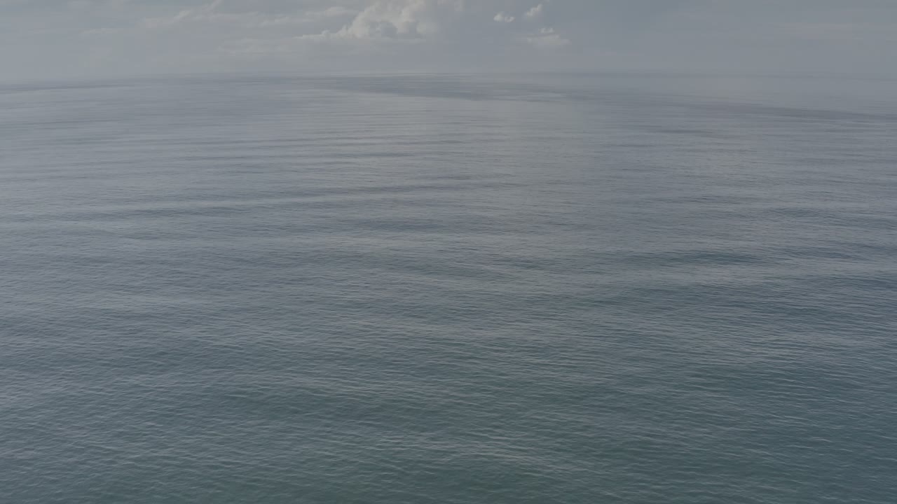 Calm ocean water under a muted sky with scattered clouds.