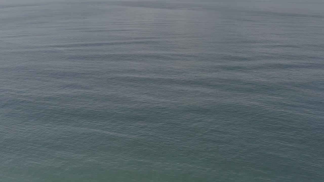 Muted green-gray water in Los Cabos, Mexico shows soft surface ripples and darker streaks, with no visible people.
