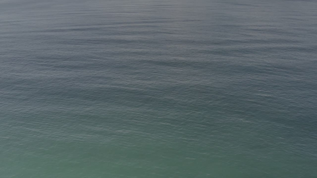At 0:01, the Los Cabos sea surface remains tightly framed, with fine ripples and a horizontal shift from blue-gray water to muted green-blue water, with no visible people.