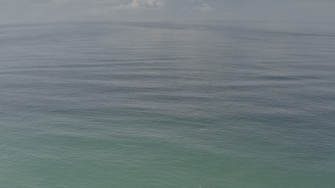 Wide view of open ocean in Los Cabos, Mexico, with a soft gray-blue sky above muted turquoise water and no visible people.