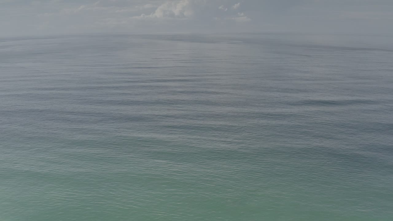 Opening frame of Los Cabos, Mexico water seen from above, with soft ripples, muted gray-blue light, a faint horizon, and no visible people.