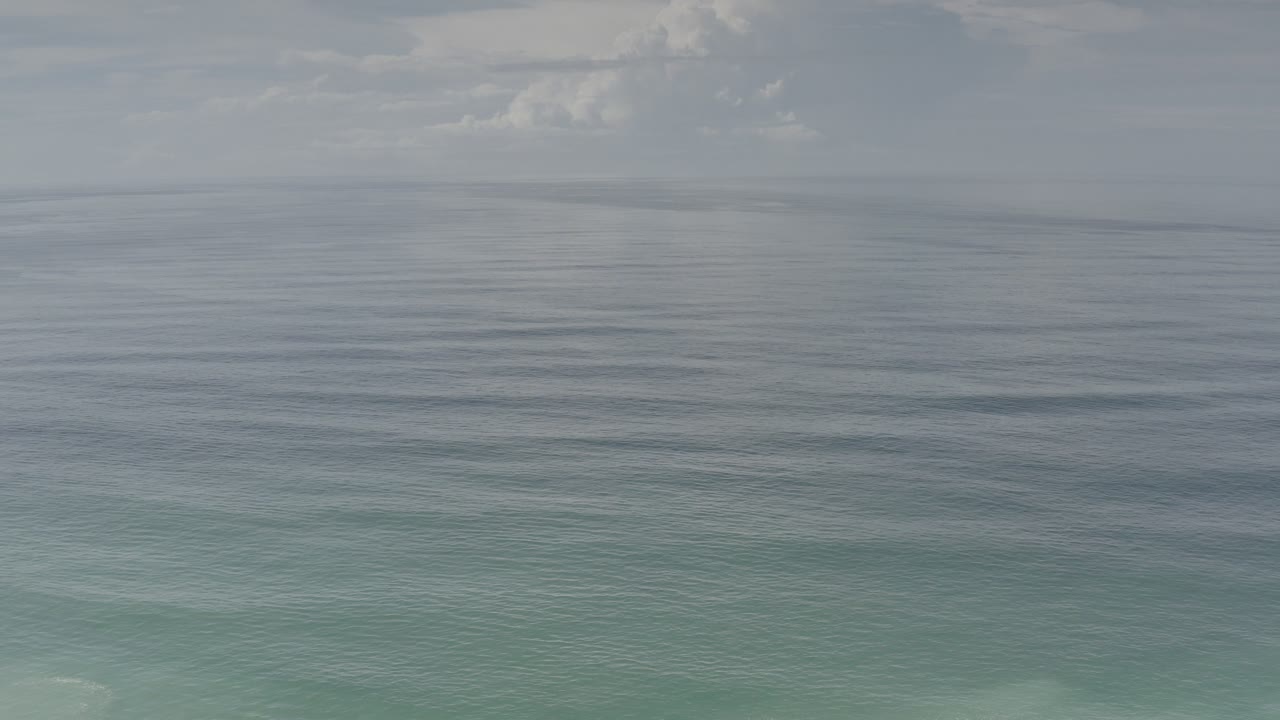 Blue green ocean under a pale cloudy sky.