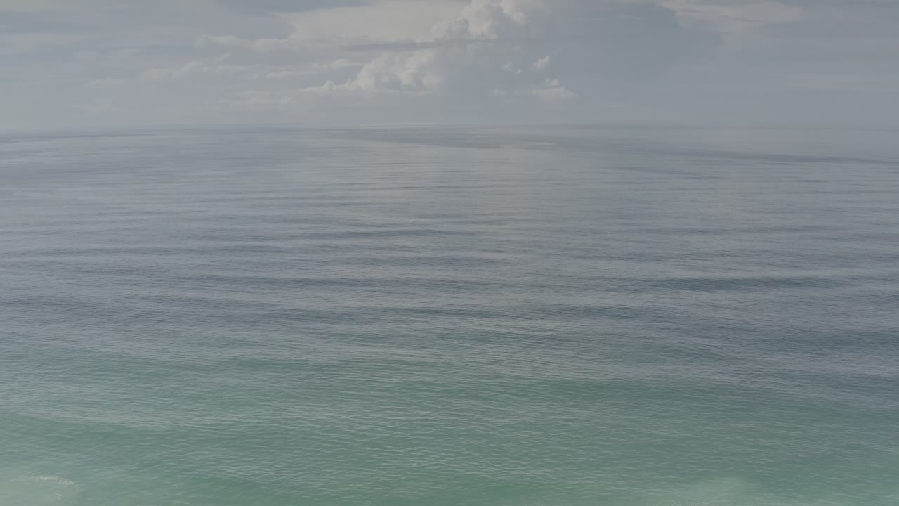 Los Cabos ocean view at one second with the horizon running across the upper frame, light cloud cover, and no visible people.