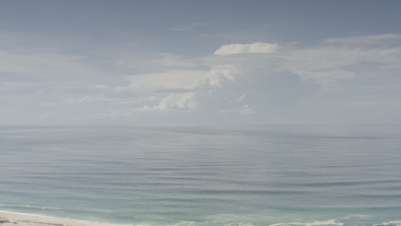 Opening frame of Los Cabos, Mexico ocean water under pale blue sky with white cloud banks and no visible people.