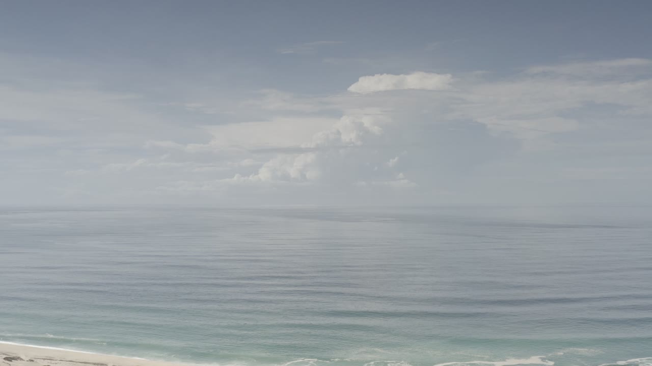 Ocean and sky with white clouds and a narrow beach edge.