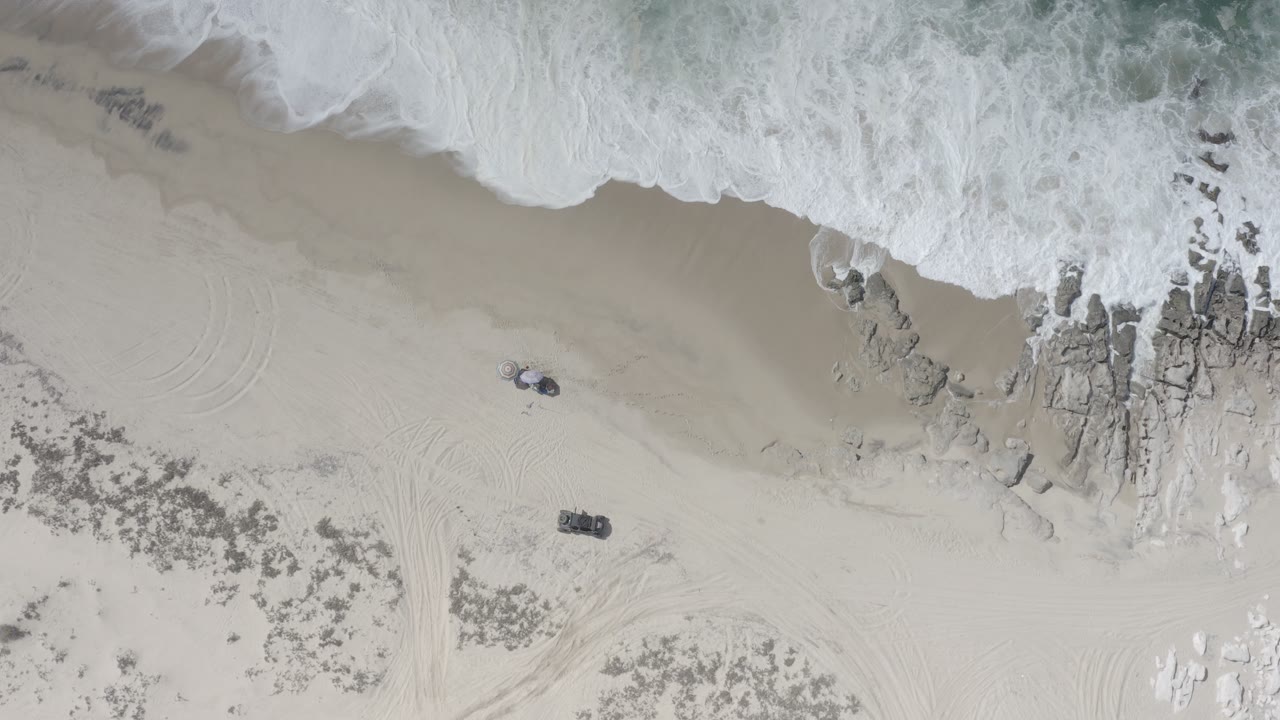 Overhead surf washing onto sand beside shoreline rocks.