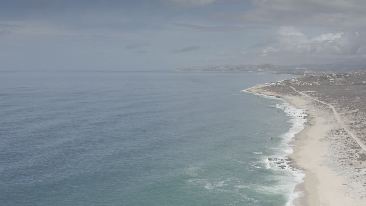 Aerial view of ocean waves meeting a sandy beach beside dunes.