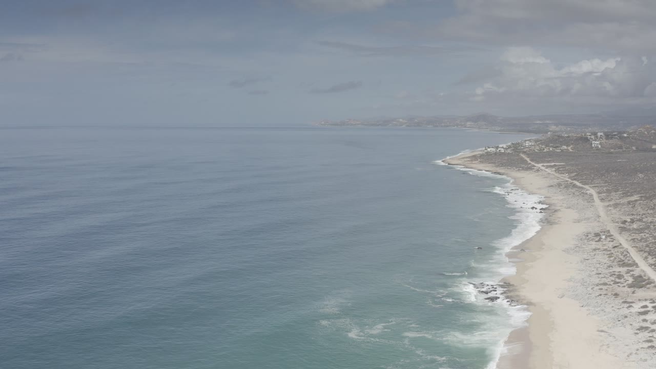 Cloudy aerial coastline with waves breaking near a pale beach.