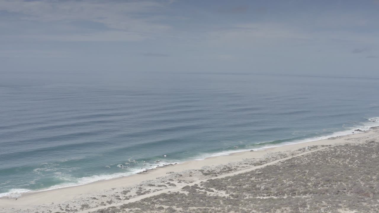 Overcast shoreline with white surf tracing the edge of the beach.