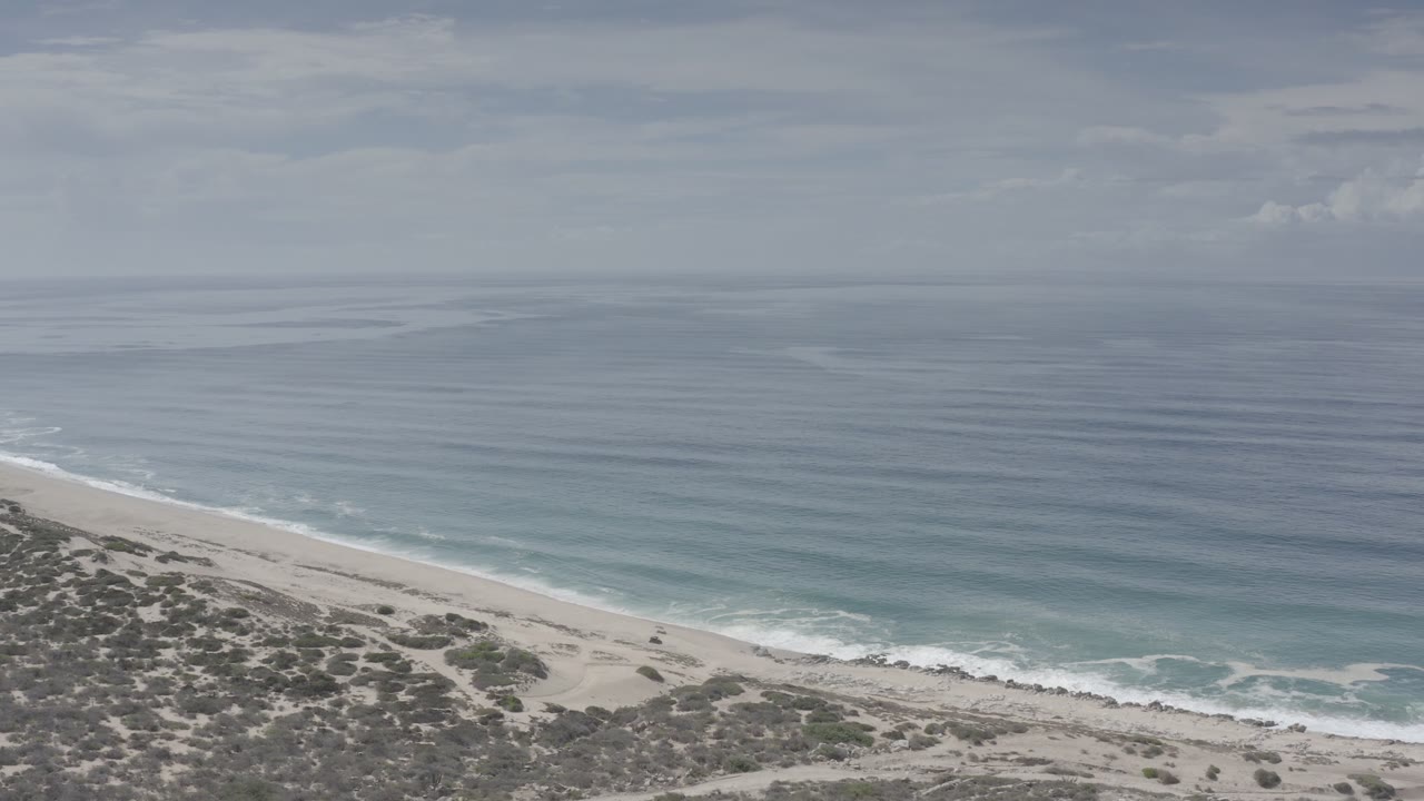 Wide elevated beach view with calm sea and low scrub foreground.