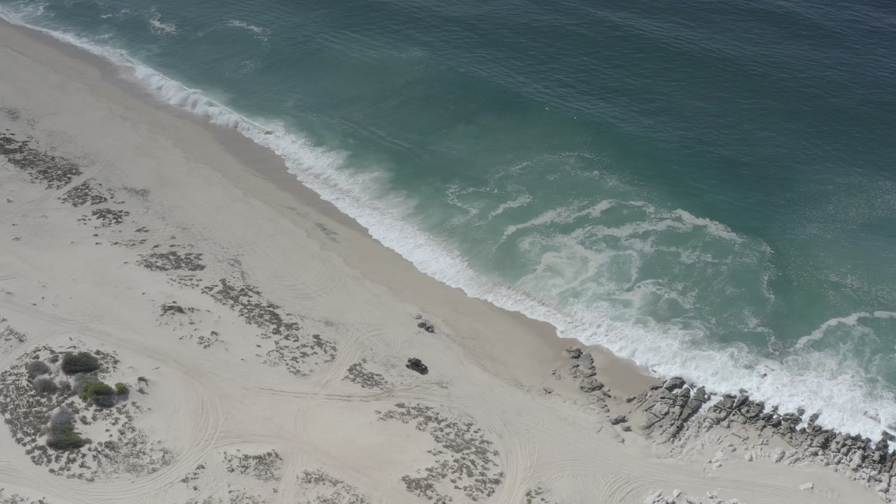 Overhead shoreline with pale sand, rocks, and green surf