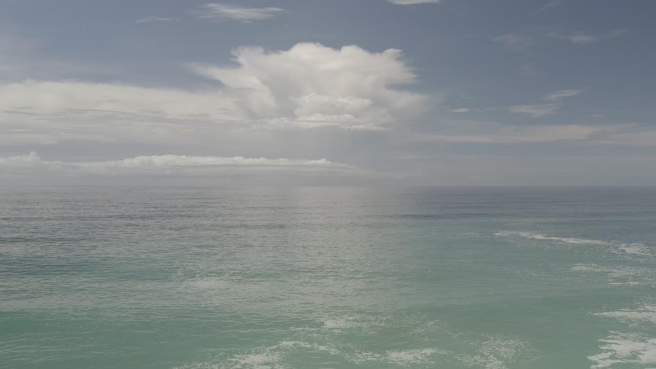 Los Cabos open water sits below a bright central cloud bank, with pale surf lines on the ocean surface and no visible people at 0:01.