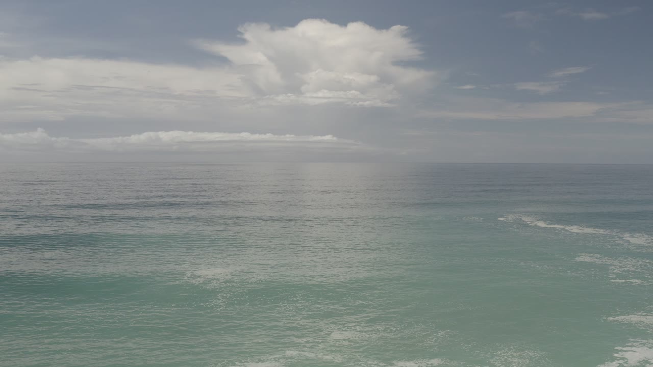 Blue-green ocean below a clouded sky and level horizon.