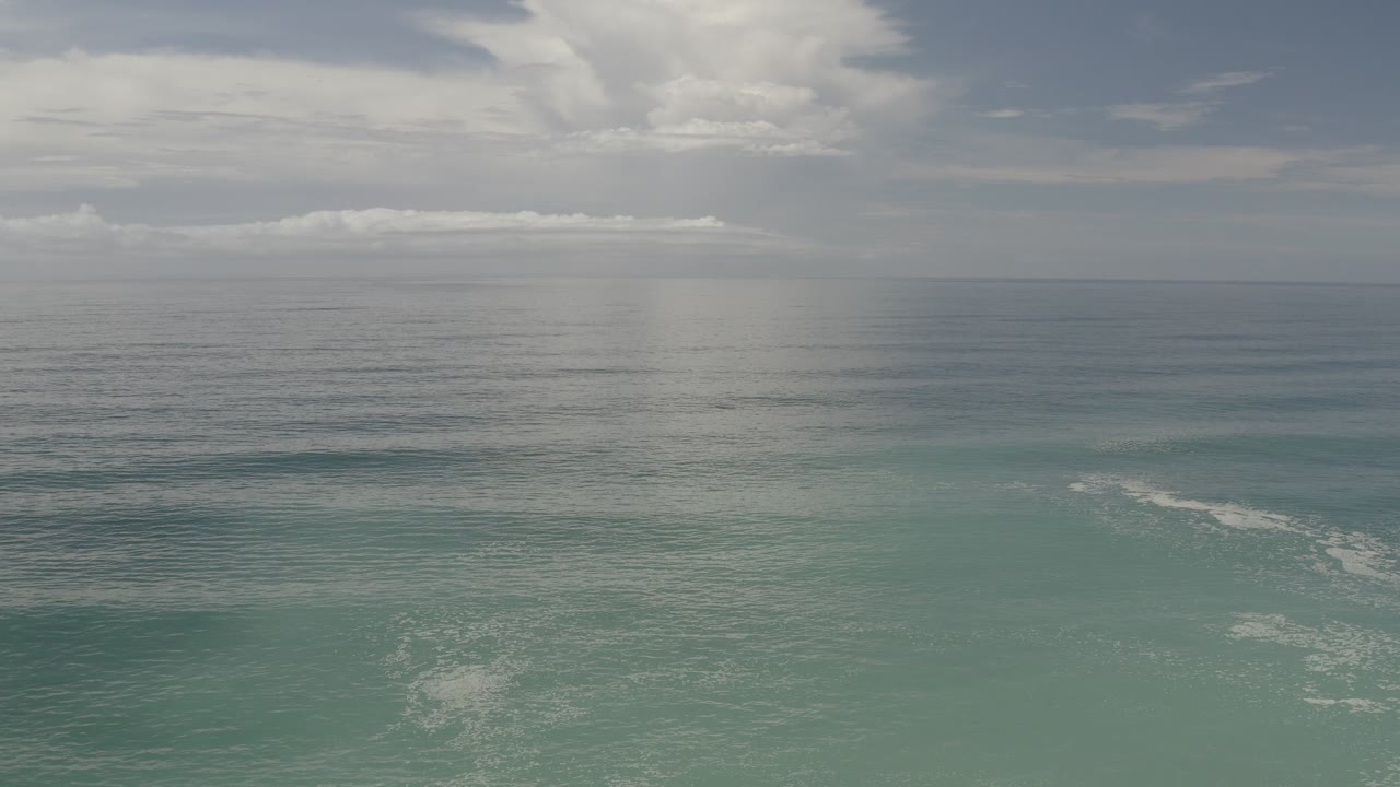 Opening frame of Los Cabos ocean water with a straight horizon, layered cloud cover, pale turquoise foreground water, and no visible people.