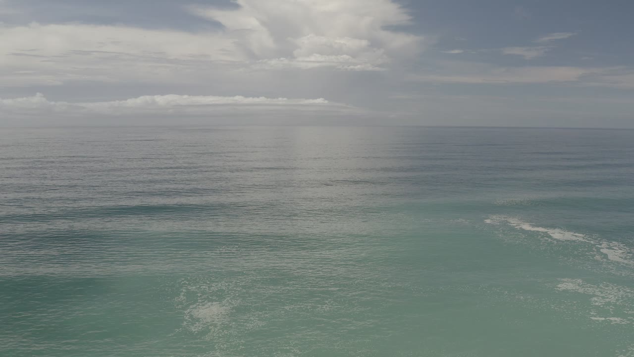 Los Cabos ocean view one second in, with calm gray water, a cloud bank over the horizon, faint rain haze, and no visible people.