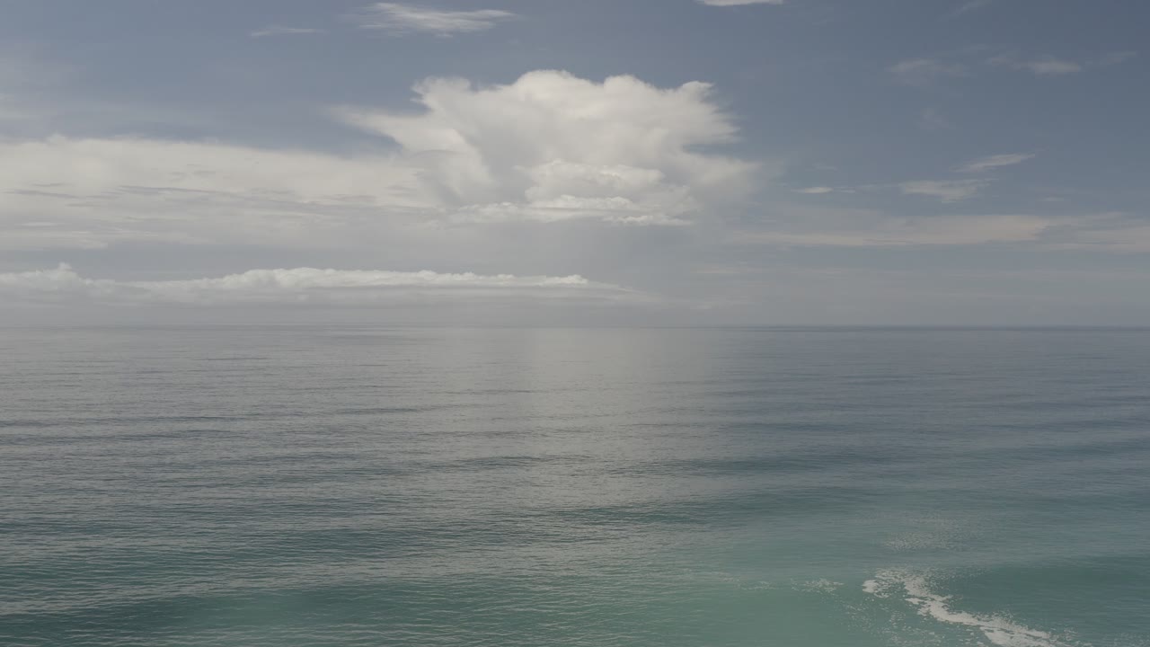 Los Cabos ocean view at the start of the clip, with a wide cloud bank above a calm horizon, blue-green water below, and no visible people.