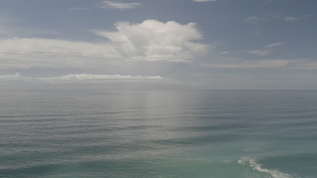 Los Cabos coastal frame with bright white clouds centered above the horizon, a pale reflection on the water, and no visible people.